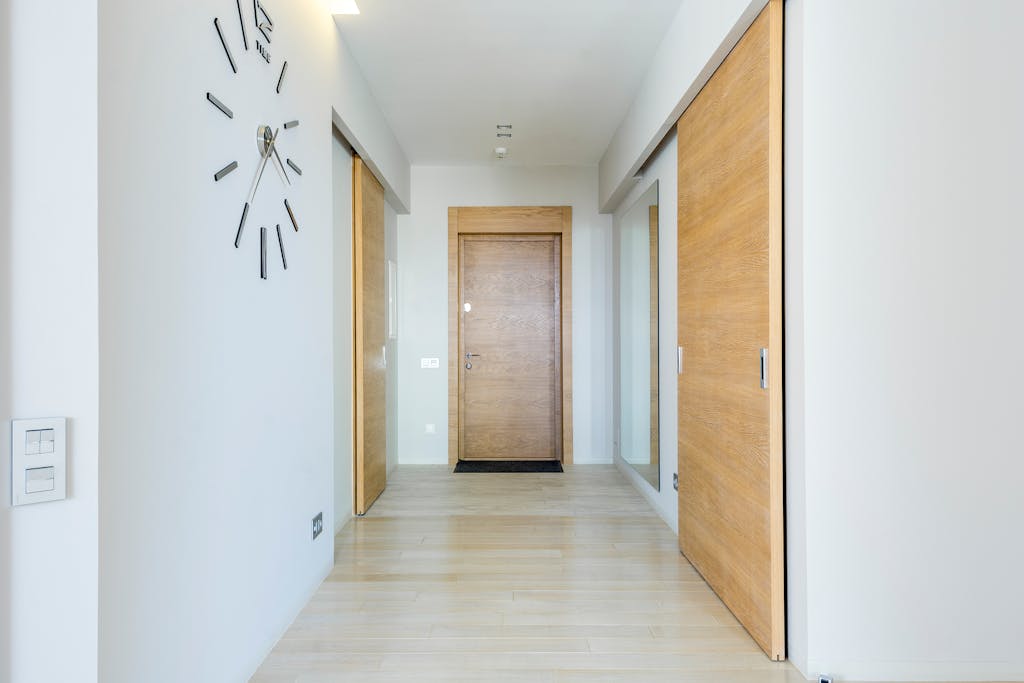Bright minimalist hallway with wooden doors and modern clock, showcasing sleek interior design.