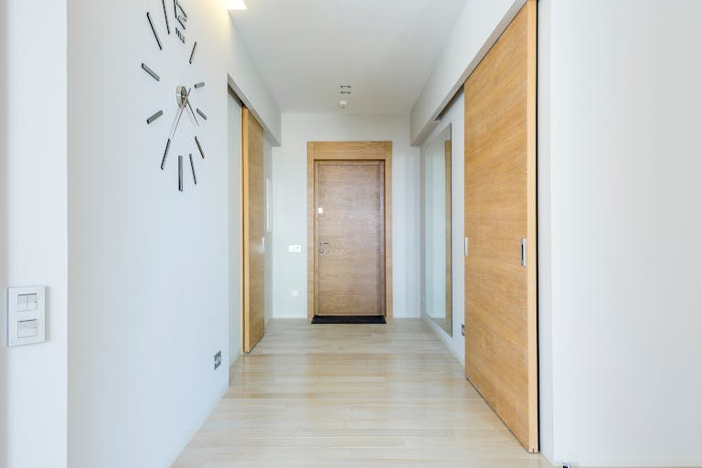 Bright minimalist hallway with wooden doors and modern clock, showcasing sleek interior design.