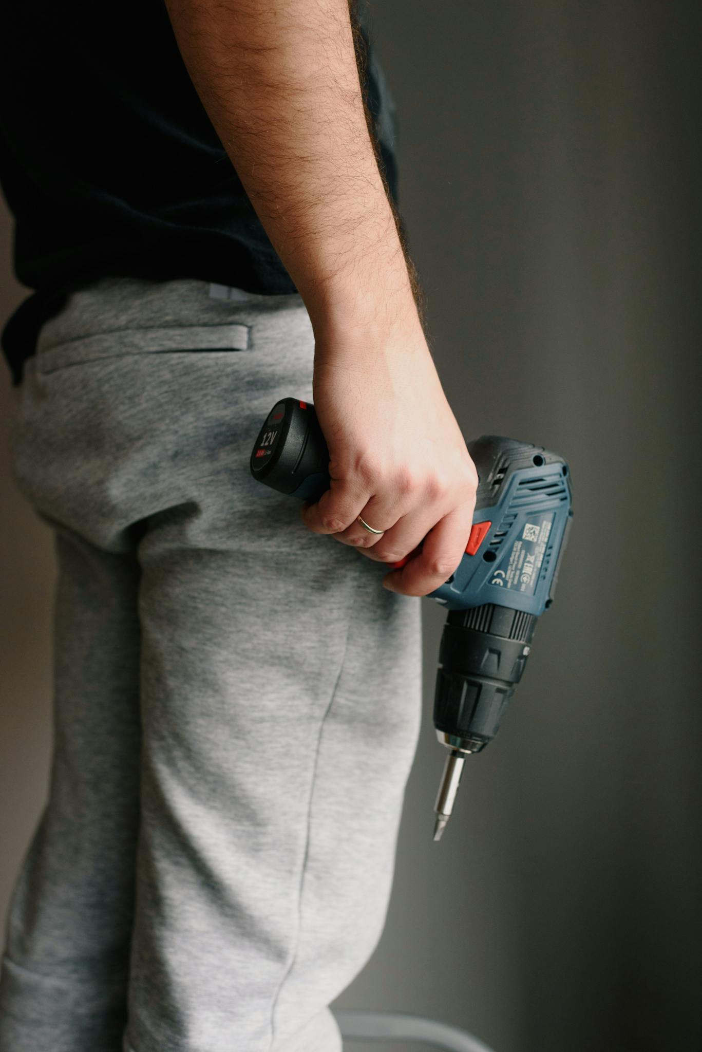 Crop anonymous male in casual clothes holding drill while renovating interior of apartment