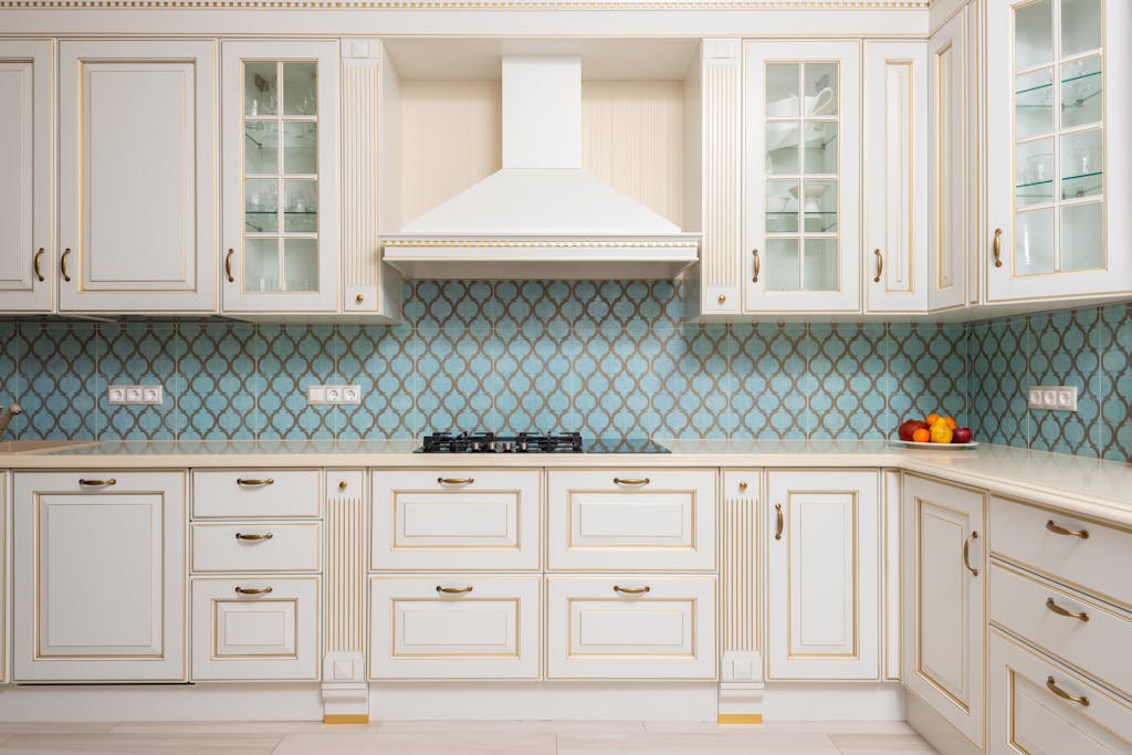 Interior of light modern kitchen with wooden white cabinets and blue tile backsplash with classic hood